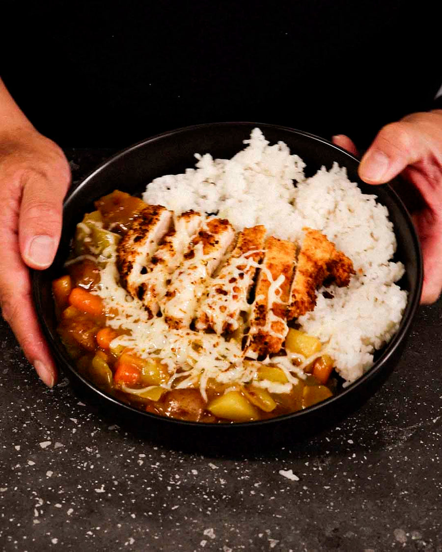 A black bowl filled with white rice and golden-brown chicken katsu, with rich Japanese curry.