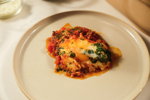 Overhead shot of Claypot Shakshuka with eggs poached in spiced tomato sauce, cooked in the Magnifique Claypot Cooker and garnished with herbs.
