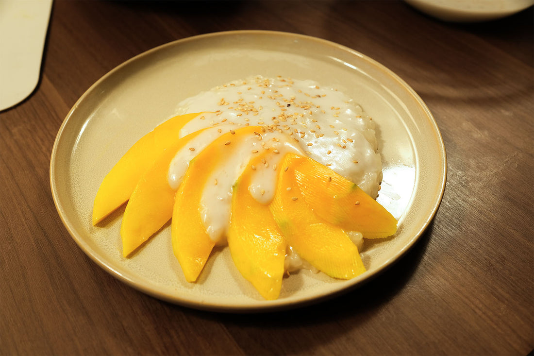 Claypot Mango Sticky Rice served with fresh sliced mango, creamy coconut sauce, and sesame seed garnish.