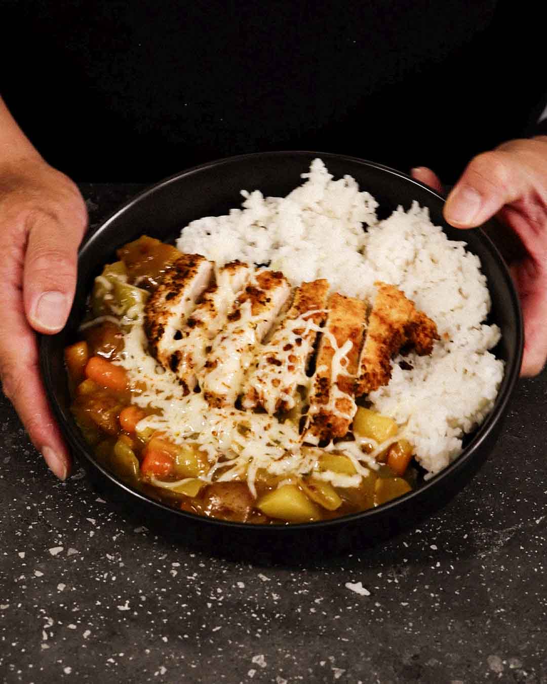 A black bowl filled with white rice and golden-brown chicken katsu, with rich Japanese curry.