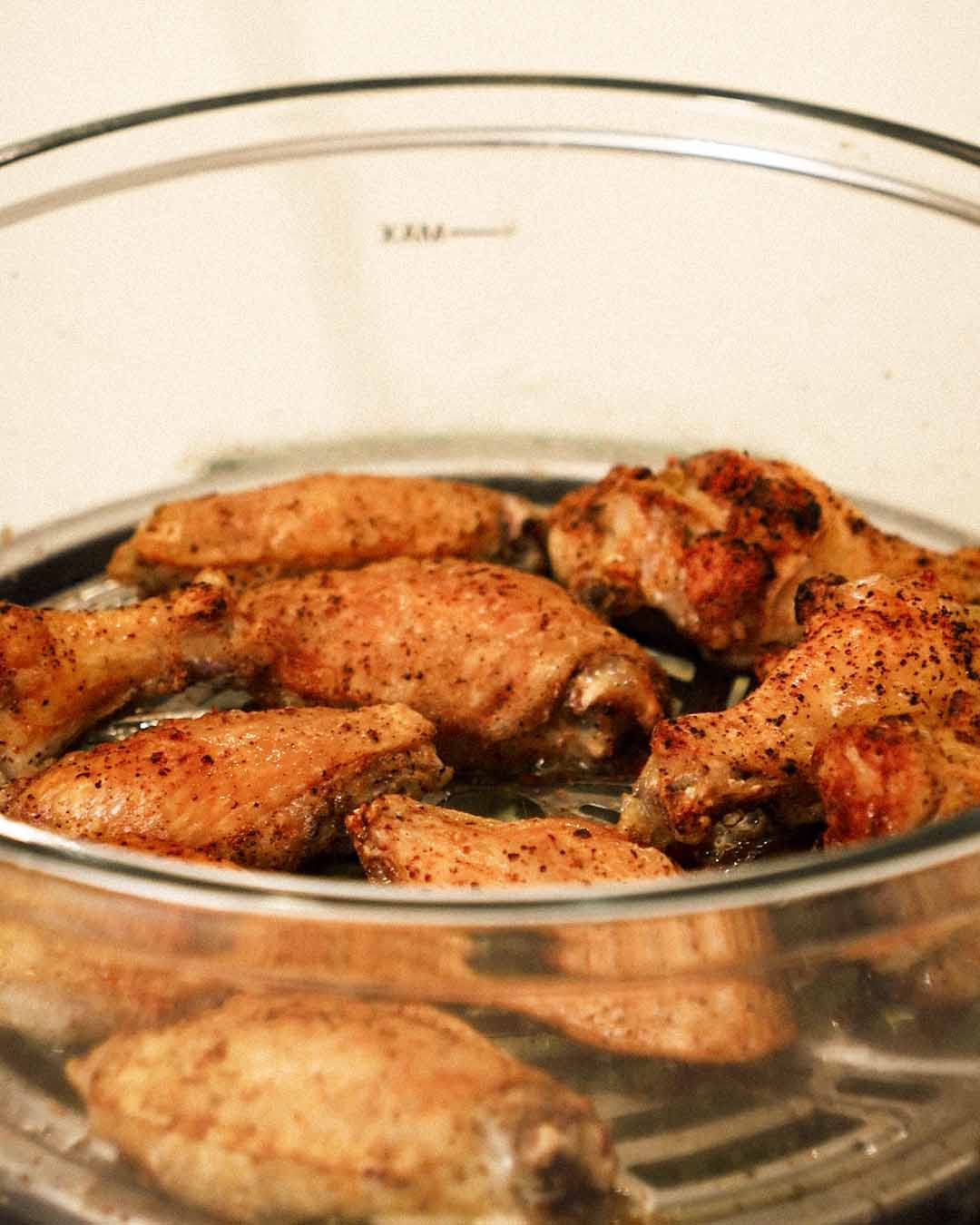 Seasoned chicken wings arranged in the glass pot, coated in spices and ready to cook.