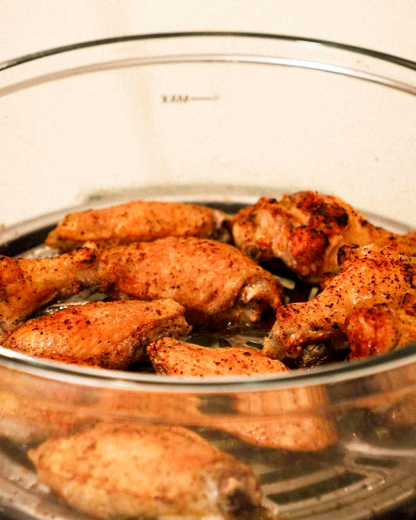 Seasoned chicken wings arranged in the glass pot, coated in spices and ready to cook.