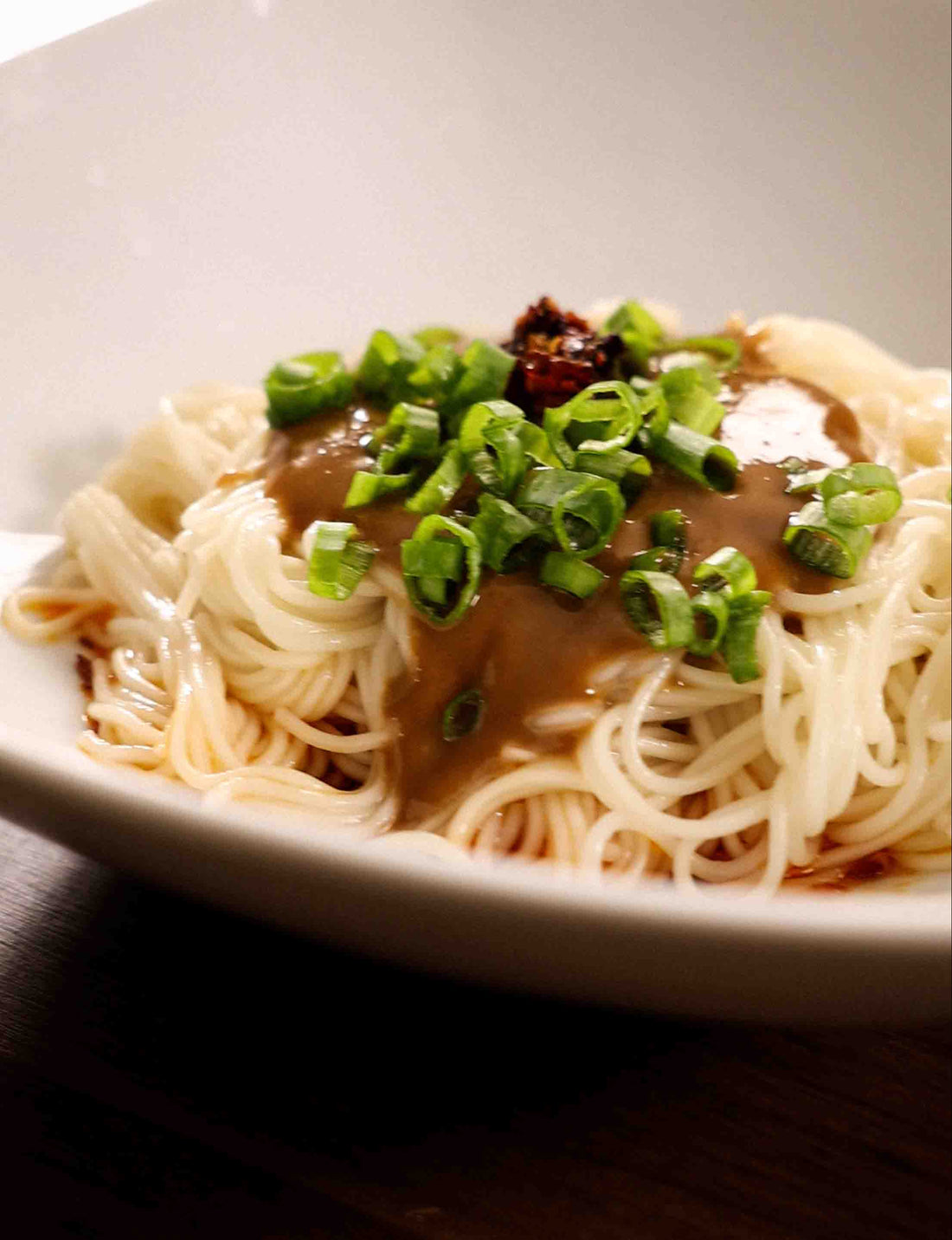 A bowl of Spicy Sesame Paste Noodles under dramatic lighting.