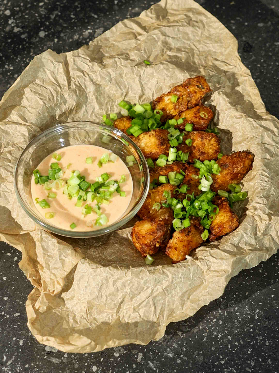 Crispy , crunchy Bang Bang Cod Bites on a parchment lined plate with tangy Bang Bang Sauce on the side. Topped with scallions. 