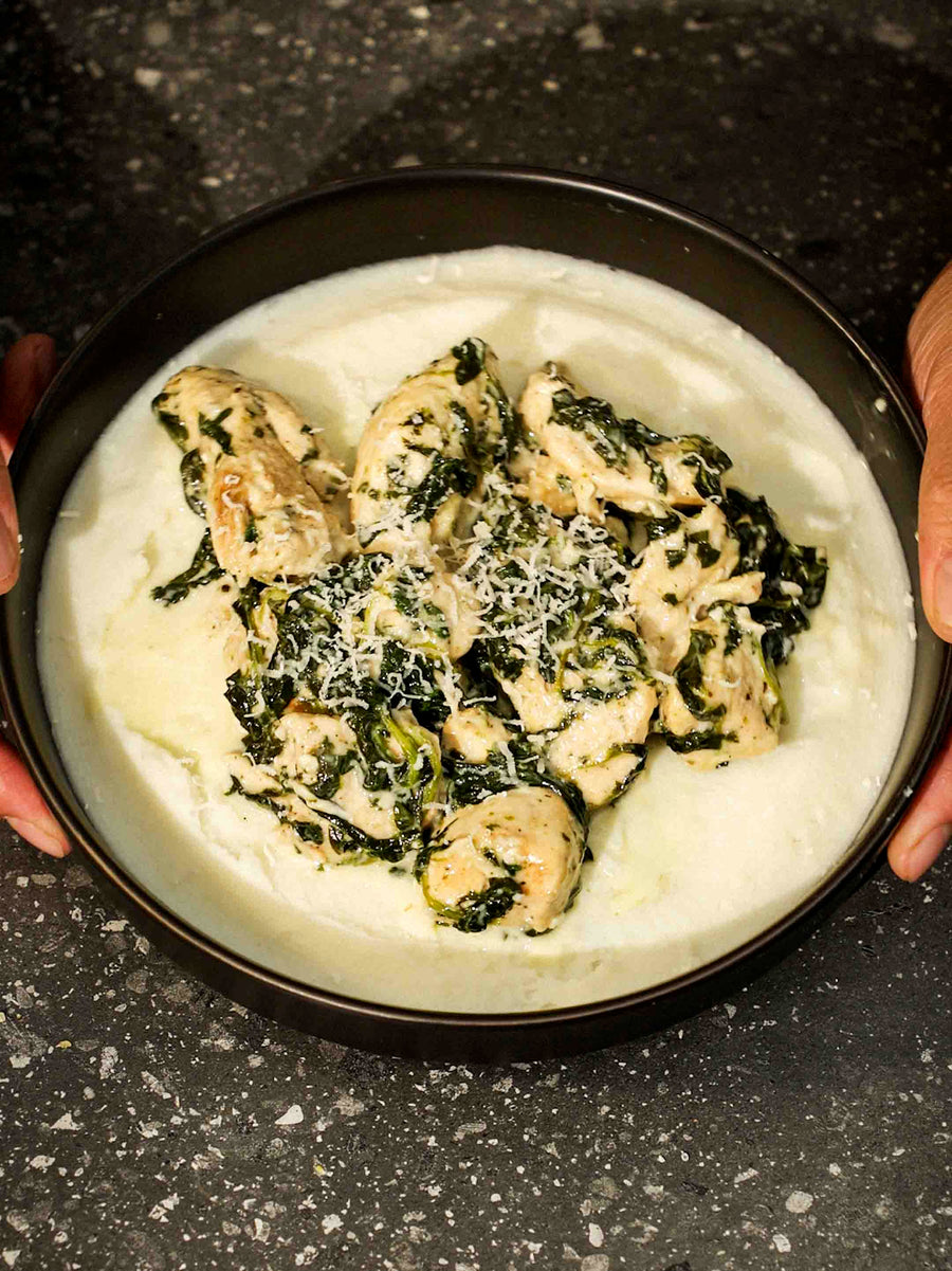 A bowl of Creamy Spinach Chicken on top of a spread of mash potatoes. Made using the Magnifique Round Claypot Multi-Cooker