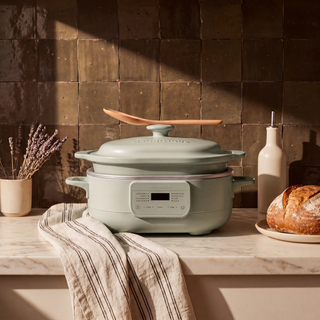 6 quart Sage Casserole Claypot Multi-Cooker on a kitchen counter beside bread and a linen towel