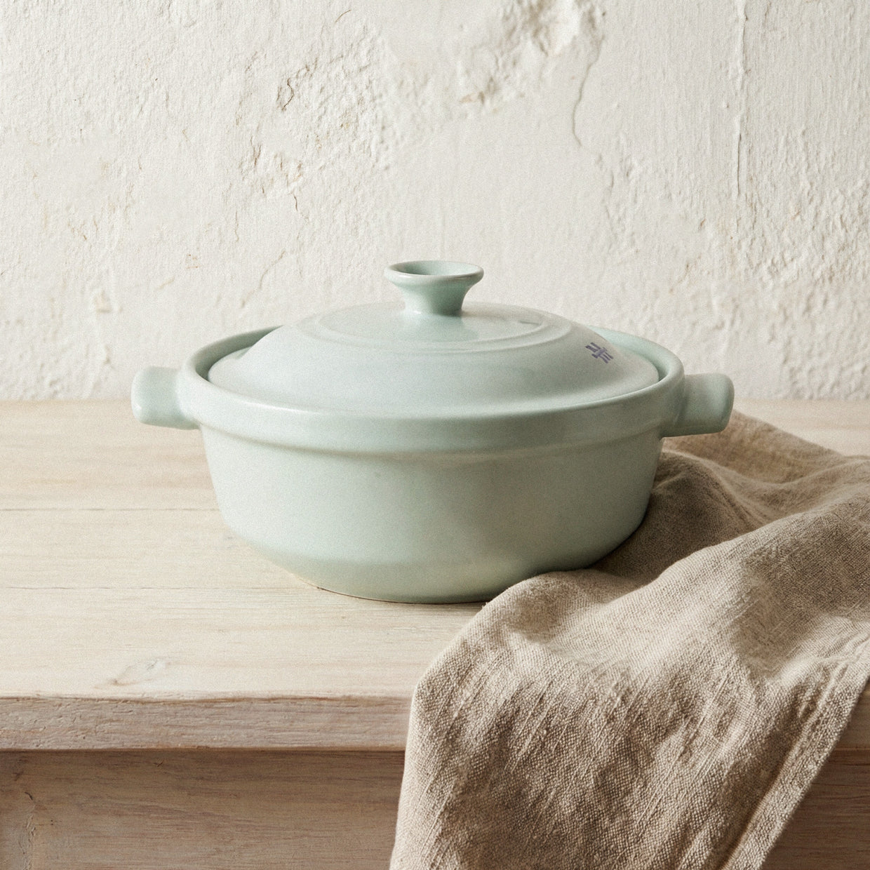 The Flami Pot, a non-toxic cookware made from pure clay, resting on a wooden surface with a linen cloth.