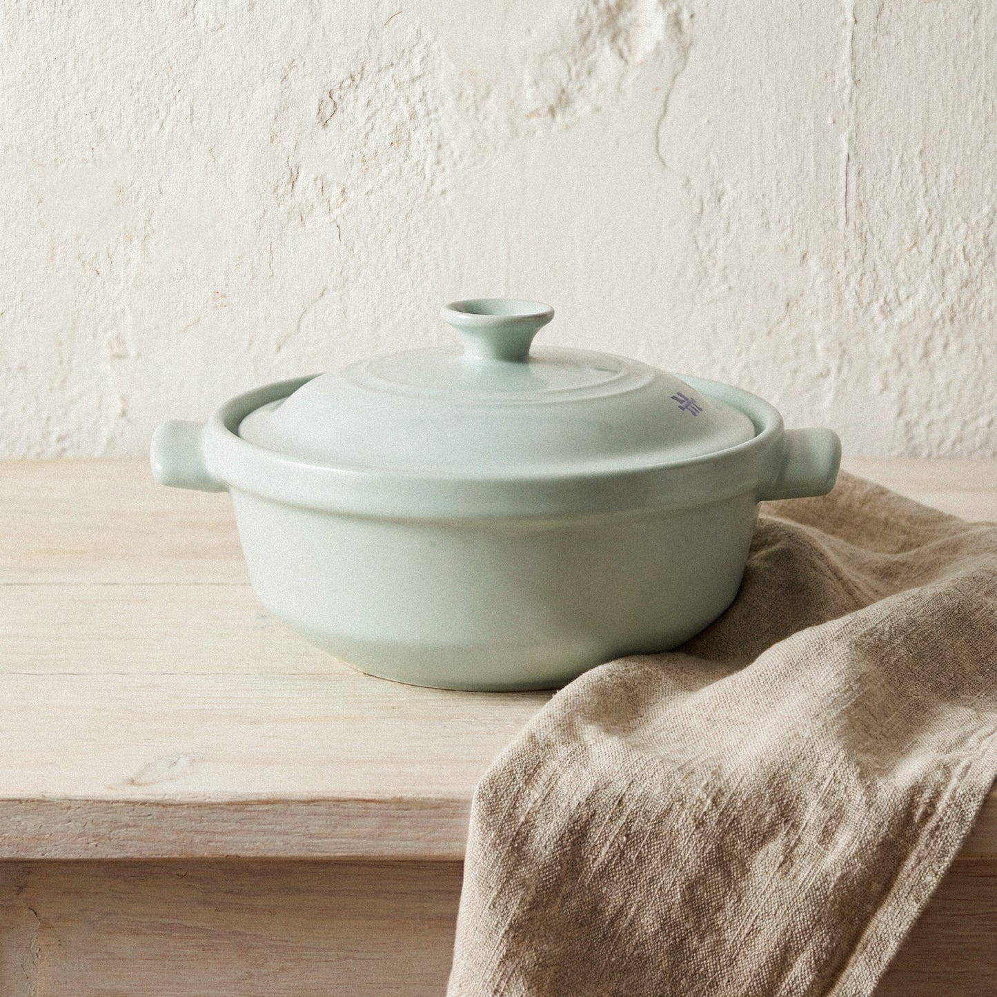 The Flami Pot, a non-toxic cookware made from pure clay, resting on a wooden surface with a linen cloth.