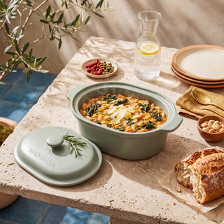 Sage Claypot pot of baked pasta on a sunny table beside plates and fresh bread