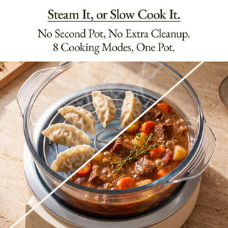 A clear glass cooking pot with a lid and handle sits on a white base on a light wood countertop. The pot is shown with food inside: dumplings on a steaming rack on the left and a stew with carrots and herbs on the right, split diagonally by a white line.