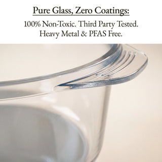 Close-up of a clear glass measuring cup with a pouring spout, with text at the top reading 'Pure Glass, Zero Coatings: 100% Non-Toxic. Third Party Tested.